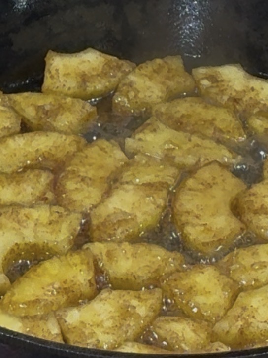 Slices of potatoes with seasoning are frying in hot oil in a dark pan, creating bubbles around the edges as they cook.