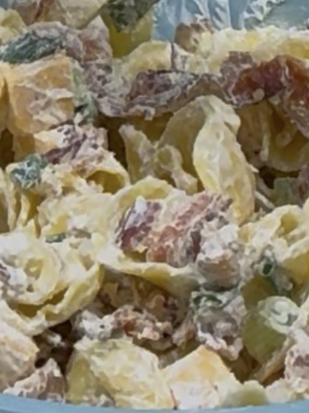 A close-up of pasta salad with shell-shaped pasta, diced tomatoes, green peppers, and a creamy dressing.