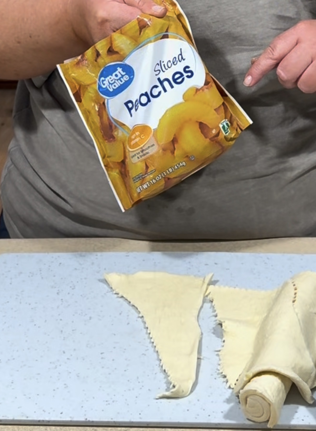 A person holds a bag of Great Value sliced peaches above a table with unrolled crescent dough triangles laid out, ready for preparation.