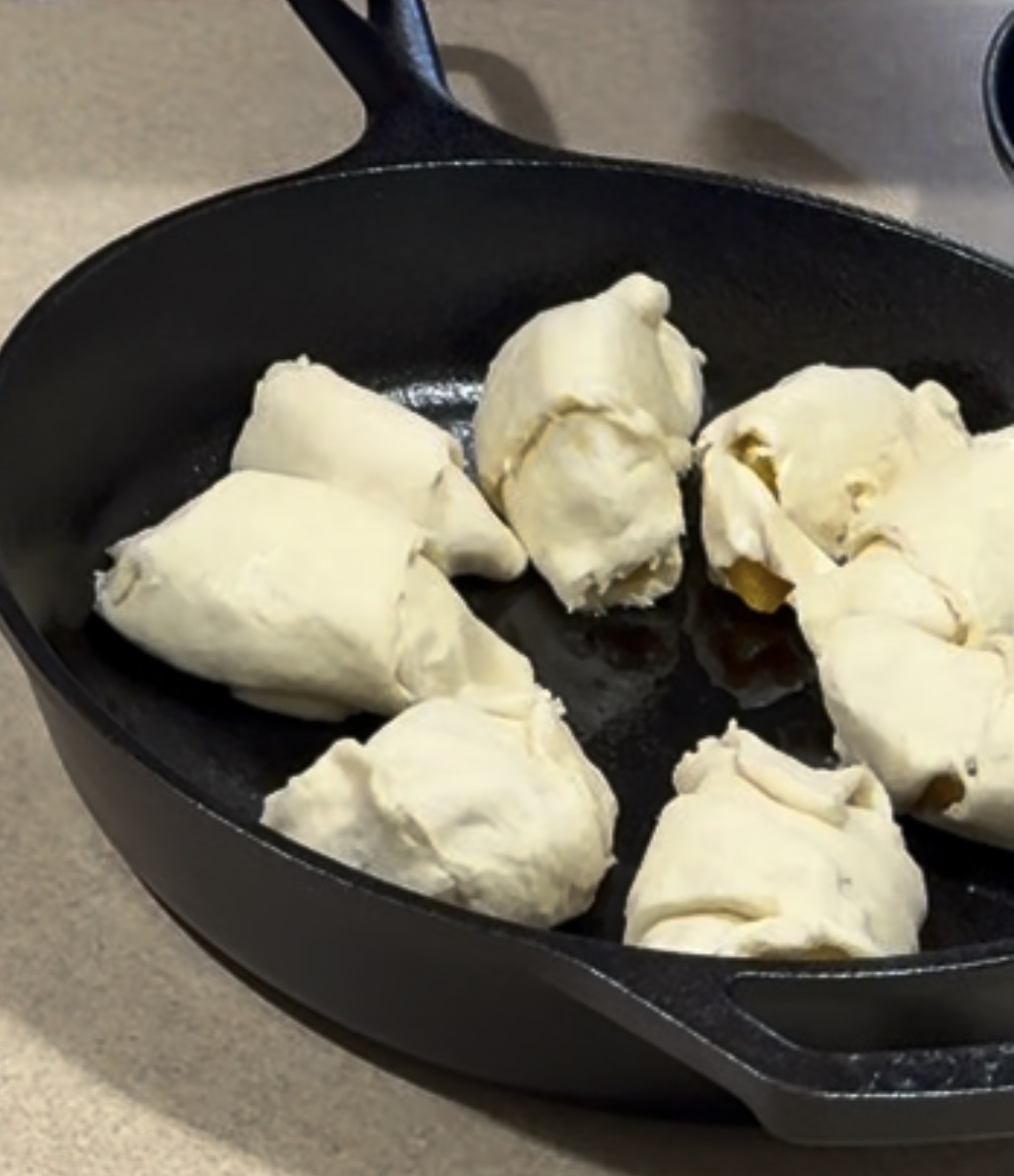 Unbaked dough-wrapped pieces arranged in a black cast iron skillet, placed on a beige countertop.