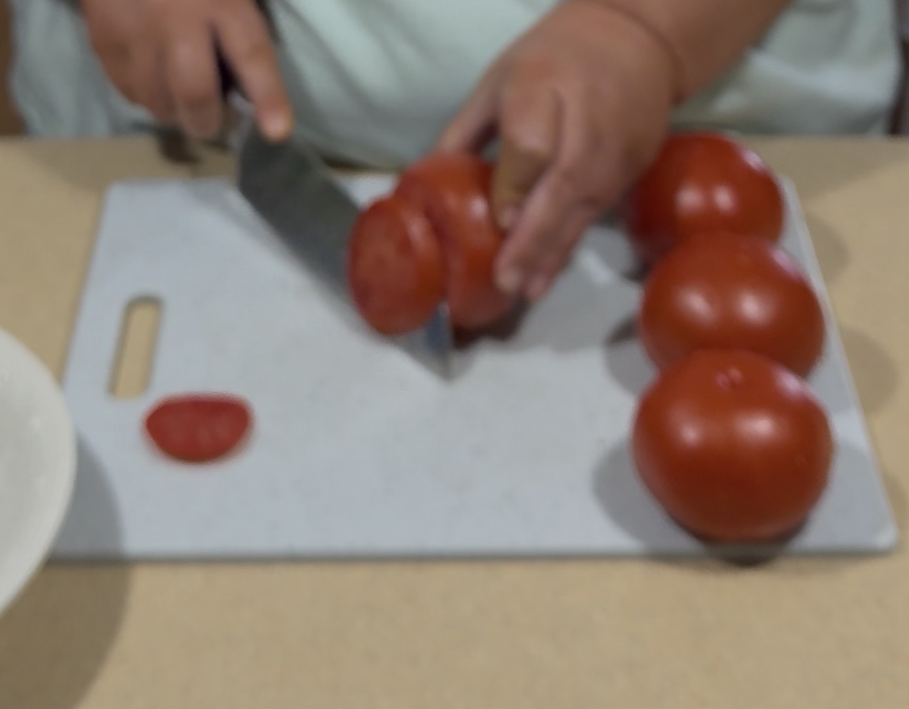 A person slicing tomatoes on a white cutting board with a knife; several whole tomatoes are on the board.