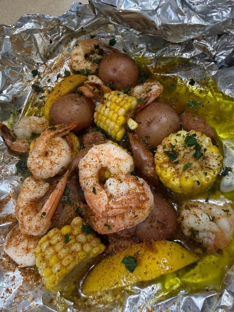 Cooked shrimp, corn on the cob slices, red potatoes, and lemon wedges seasoned with herbs and spices, served in a foil packet with melted butter.