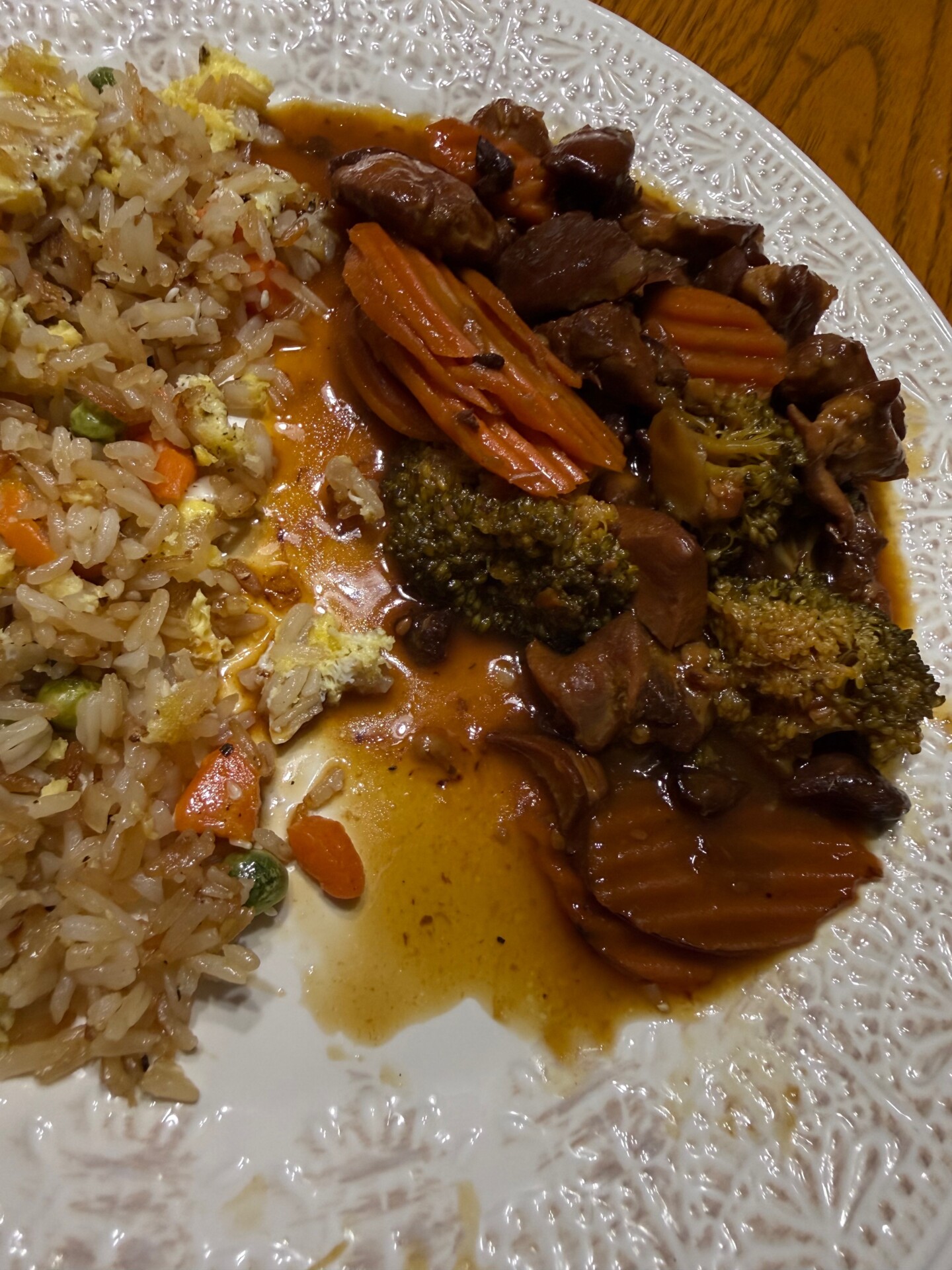 A plate of food with fried rice containing peas, carrots, and egg on the left, and a savory stir-fry with chicken, broccoli, and sliced carrots in a brown sauce on the right, on a white textured plate.