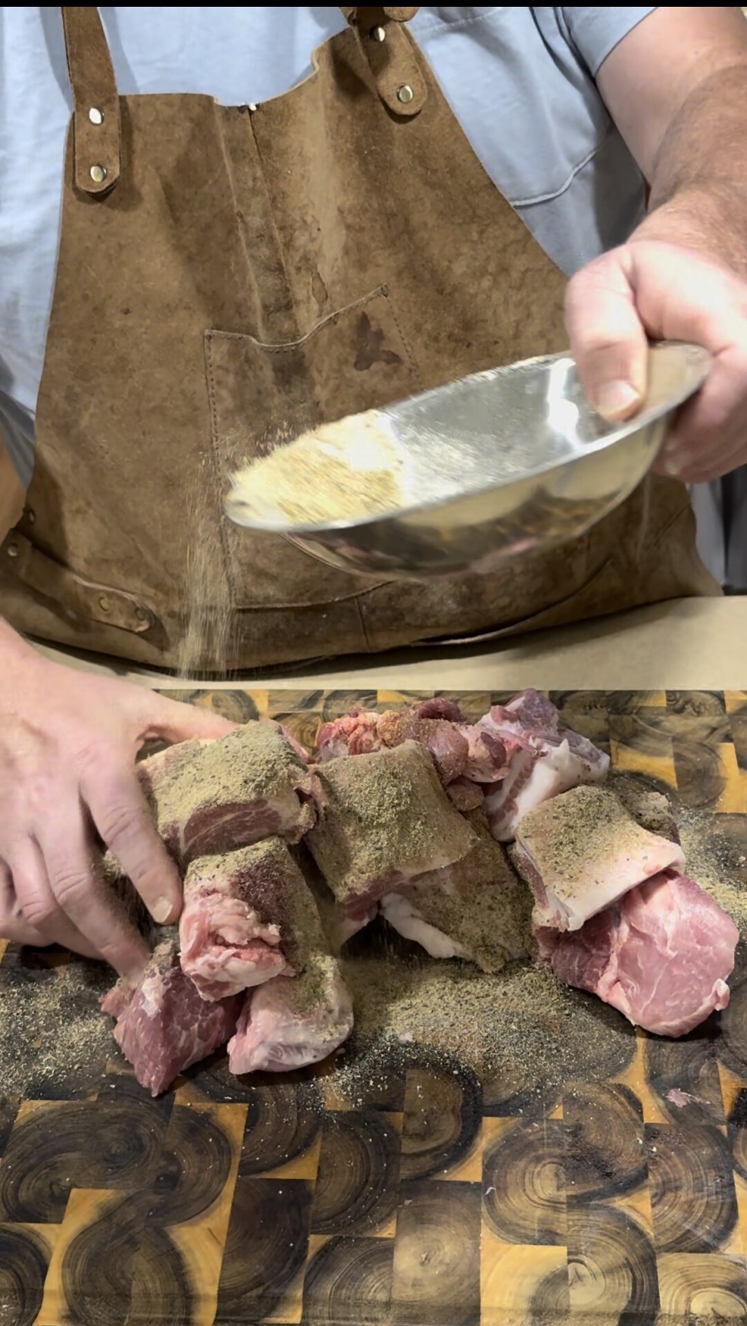 A person wearing a brown apron sprinkles seasoning from a metal bowl onto several pieces of raw meat arranged on a wooden cutting board.