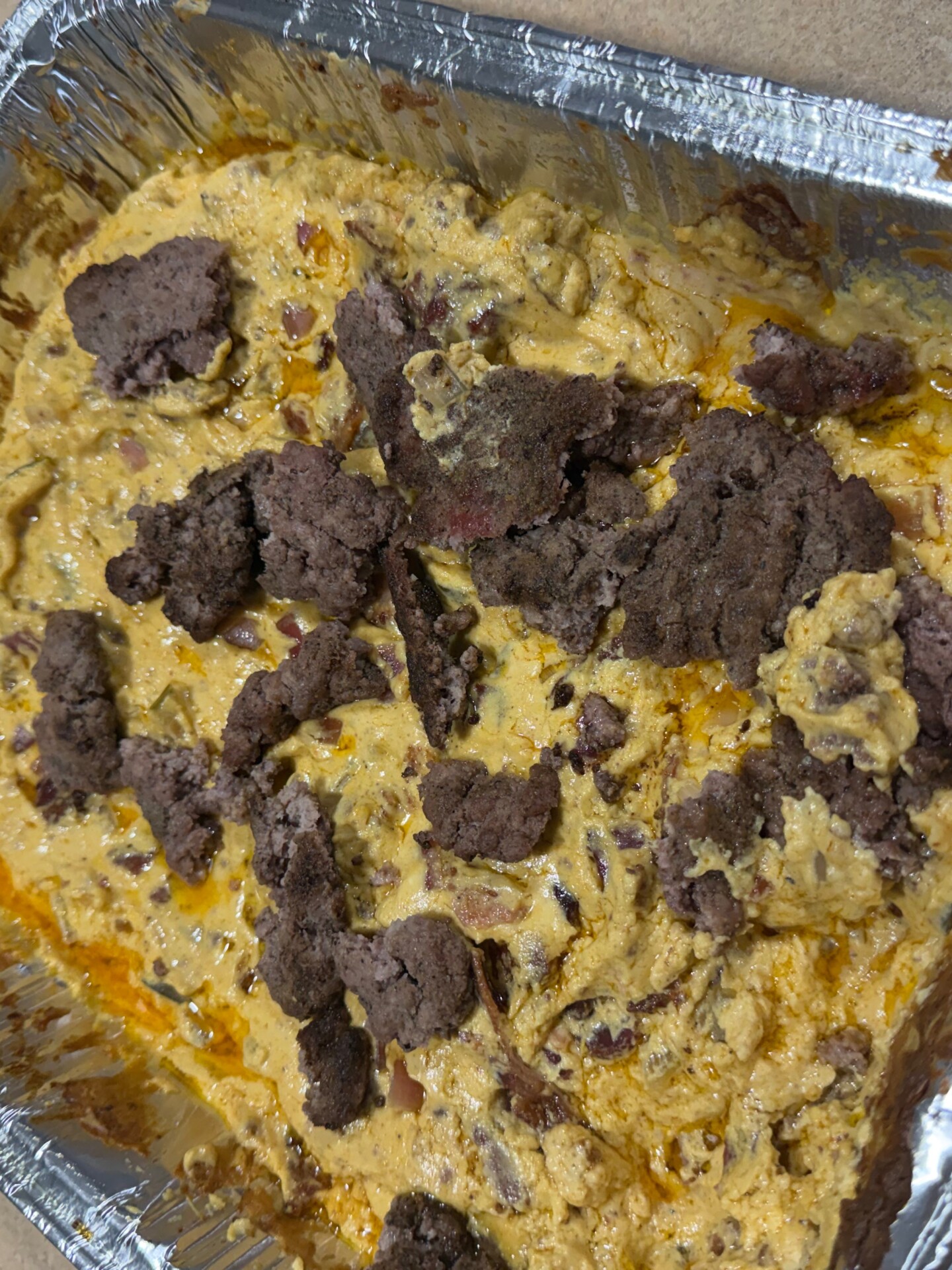 A foil baking dish filled with creamy, cheesy dip topped with crumbled ground beef.