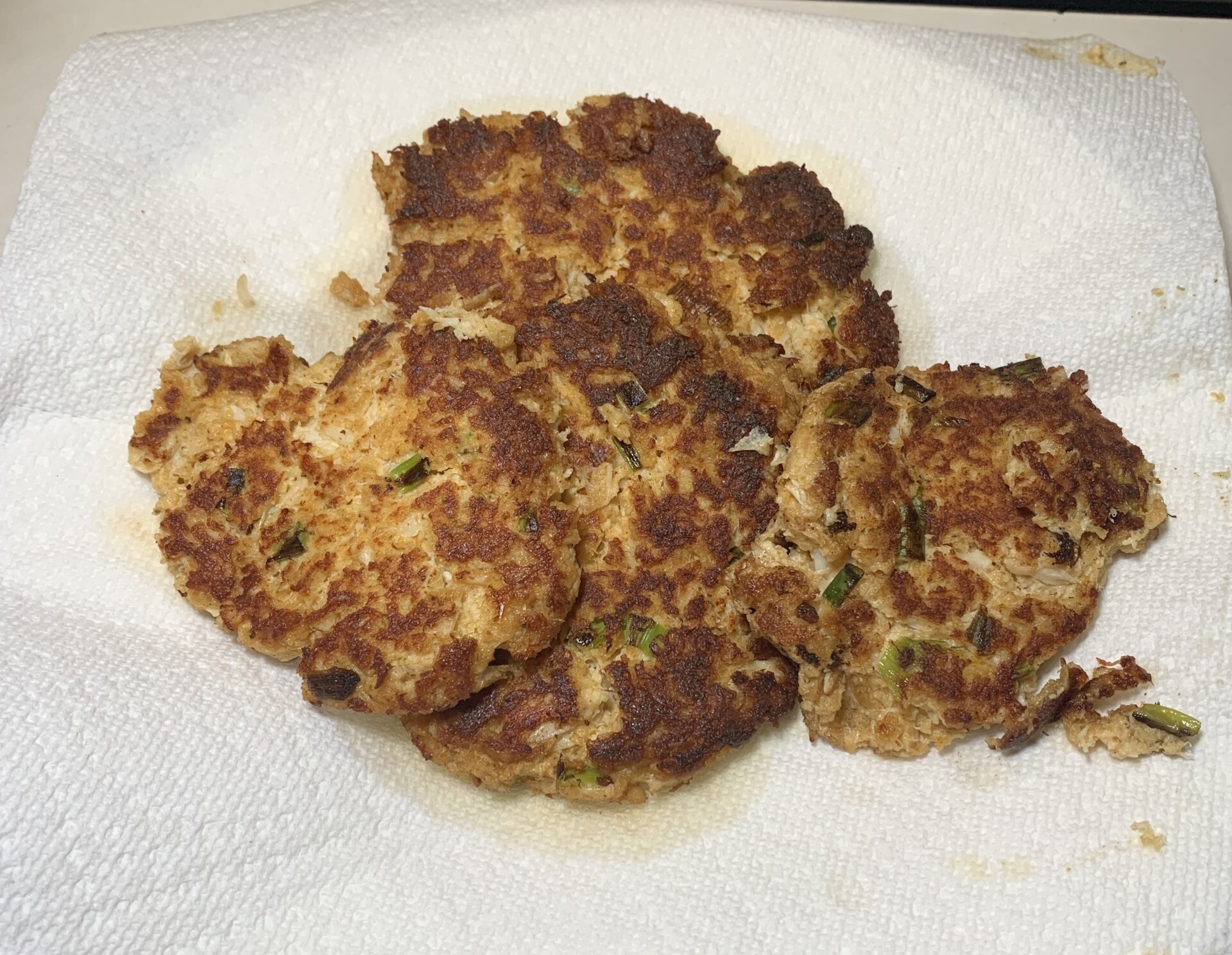 Three browned, homemade tuna patties with green herbs, resting on a white paper towel to absorb excess oil.