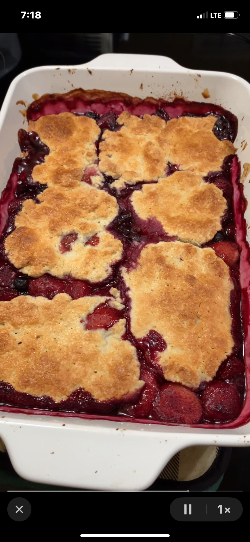 A rectangular baking dish filled with berry cobbler, featuring golden-brown biscuit topping and bubbling berry filling along the edges.