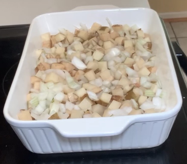 A white ceramic baking dish filled with chopped onions and diced potatoes, sitting on a stovetop, ready to be cooked.