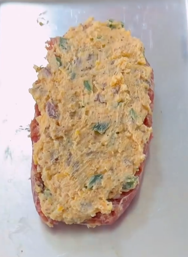 A raw, halved bell pepper on a baking tray is filled with a cheesy, seasoned mixture containing bits of green vegetables.