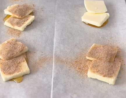 Slices of butter placed on parchment paper, some topped with a sprinkling of cinnamon sugar, and some on a drizzle of honey.