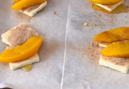 Slices of peach, pats of butter, sugar, and syrup are arranged on parchment paper, ready for baking.