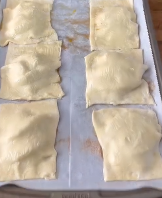 Six unbaked pastry squares are arranged on a parchment-lined baking sheet, ready to be baked. The pastries are slightly puffed and spaced evenly apart.