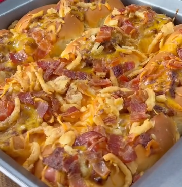 A close-up of a baking pan filled with golden-brown cheesy rolls topped with crispy bacon pieces and fried onions, fresh out of the oven.