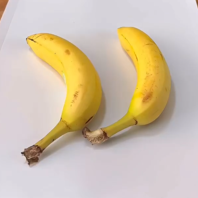 Two ripe yellow bananas with some brown spots are placed side by side on a plain white surface.