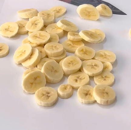 Sliced bananas are scattered on a white surface with a kitchen knife visible in the background.