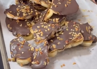 Chocolate-covered pastries with chopped nuts sprinkled on top are arranged on a sheet of parchment paper. The treats appear to have a flaky base and are broken into irregular pieces.