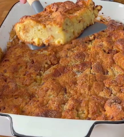 A close-up of a golden-brown baked casserole being lifted out of a white baking dish with a spatula, showing a moist and fluffy interior.