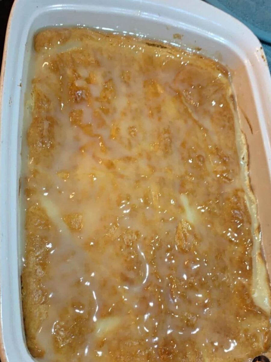 A golden-brown baked dessert in a white rectangular dish, topped with a glossy glaze or icing that covers most of the surface. The texture looks soft and slightly uneven.