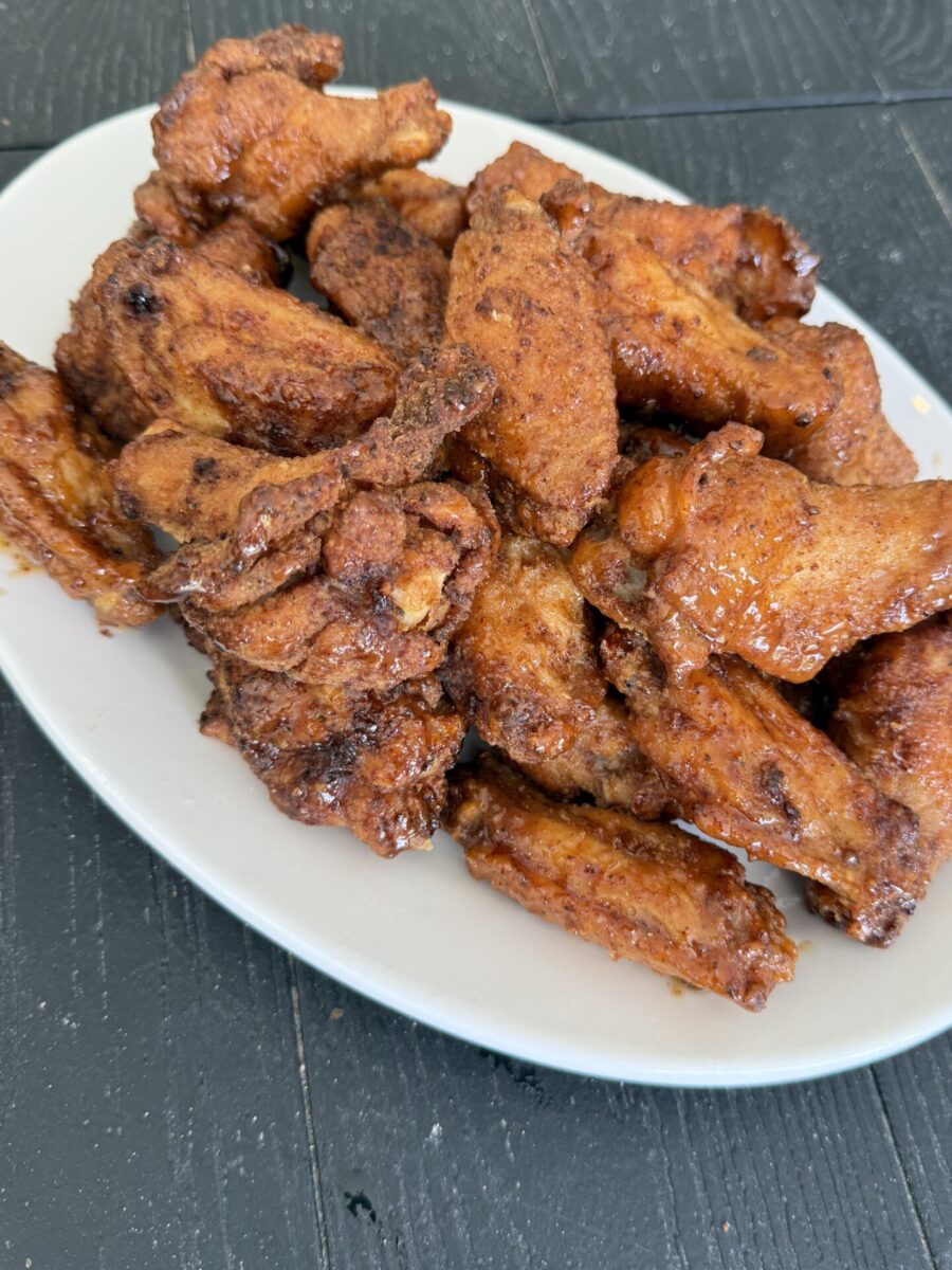 A white plate piled high with crispy, golden-brown fried chicken wings, placed on a dark wooden table.