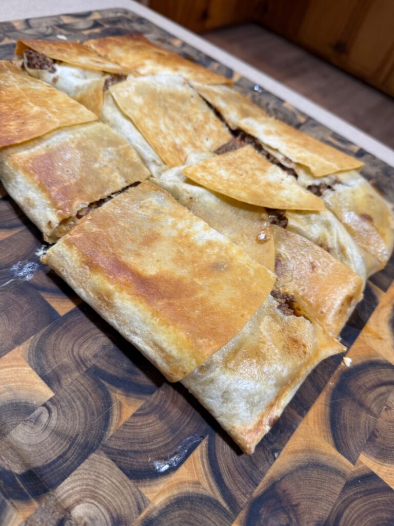 Golden, crispy, rectangular pastry pieces filled with a savory meat mixture, arranged on a wooden cutting board with a geometric pattern.