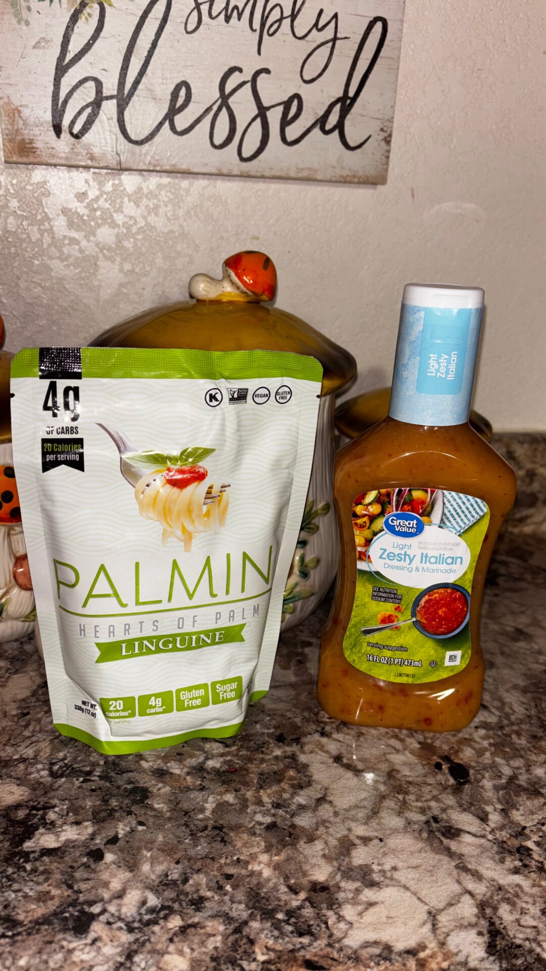 A bag of Palmini hearts of palm linguine and a bottle of Great Value zesty Italian dressing sit on a kitchen counter with decorative jars in the background.
