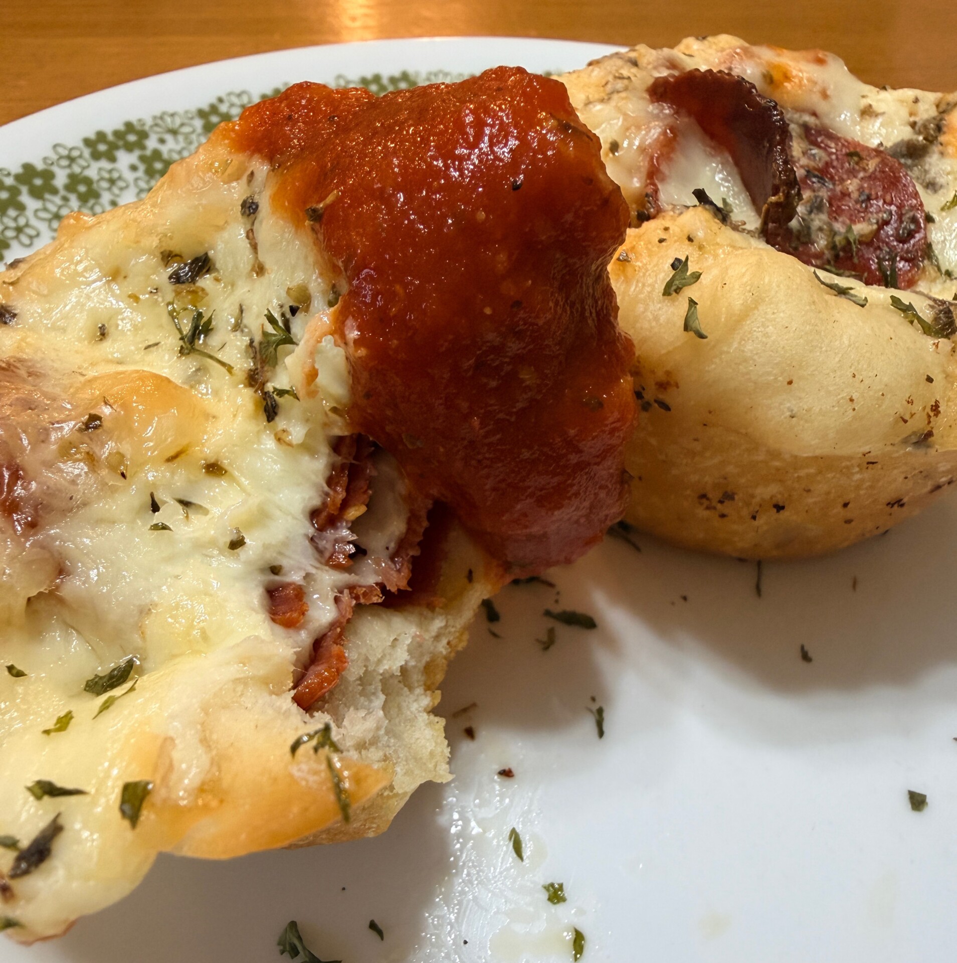 A close-up of two pieces of cheesy stuffed bread topped with tomato sauce and herbs on a white plate with a green floral border.