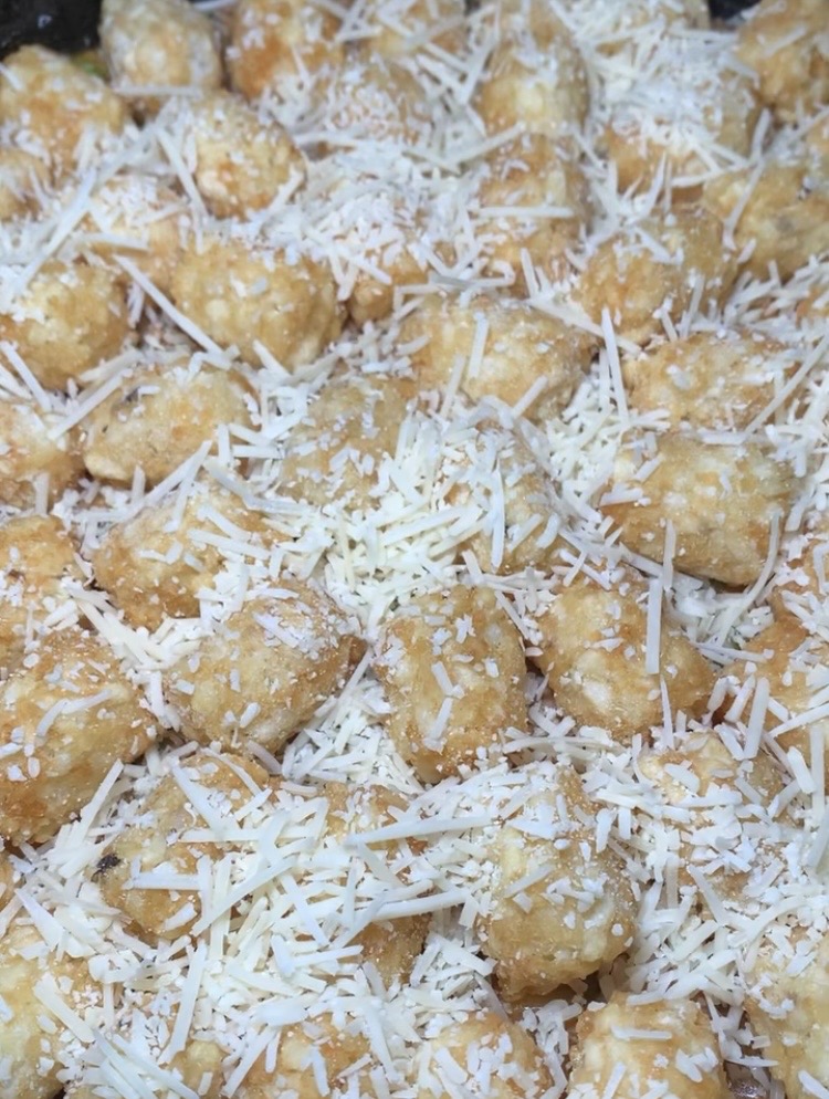 A close-up of golden tater tots generously topped with shredded white cheese, creating a textured and appetizing appearance.