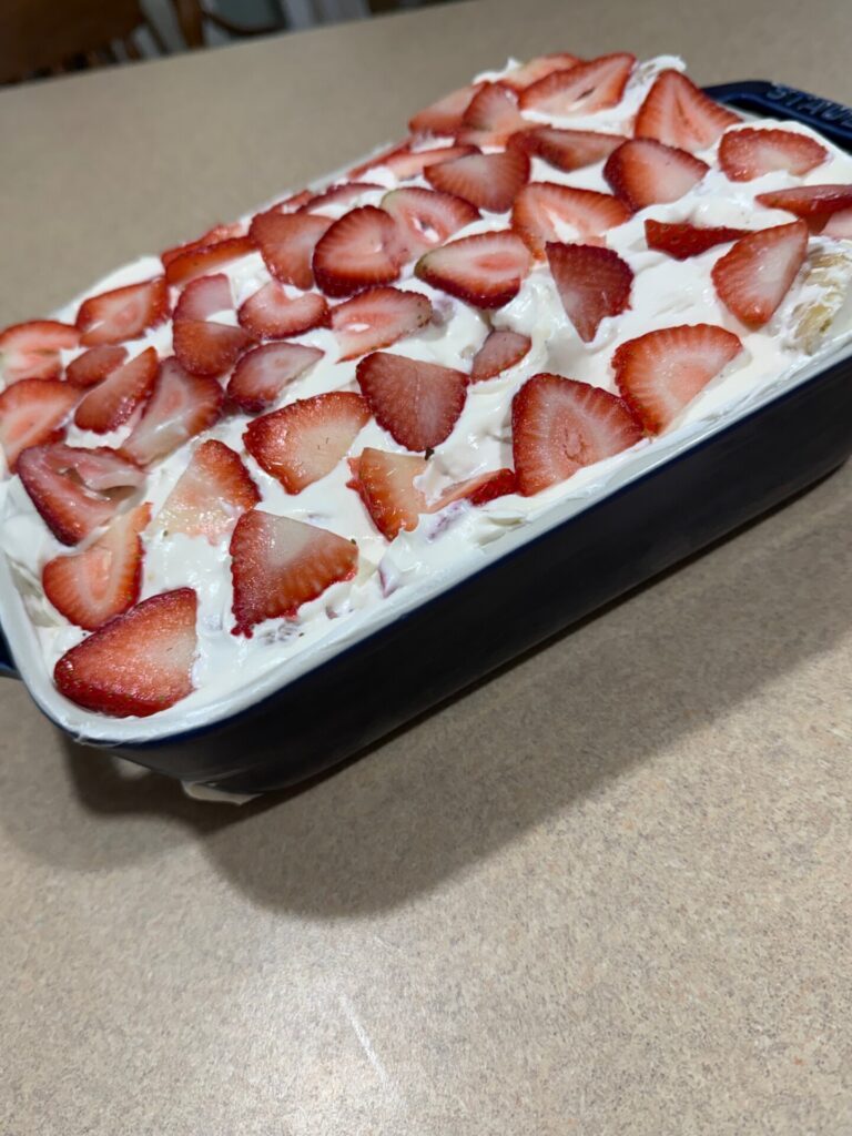 A rectangular dish filled with a creamy dessert topped with sliced strawberries sits on a kitchen counter.