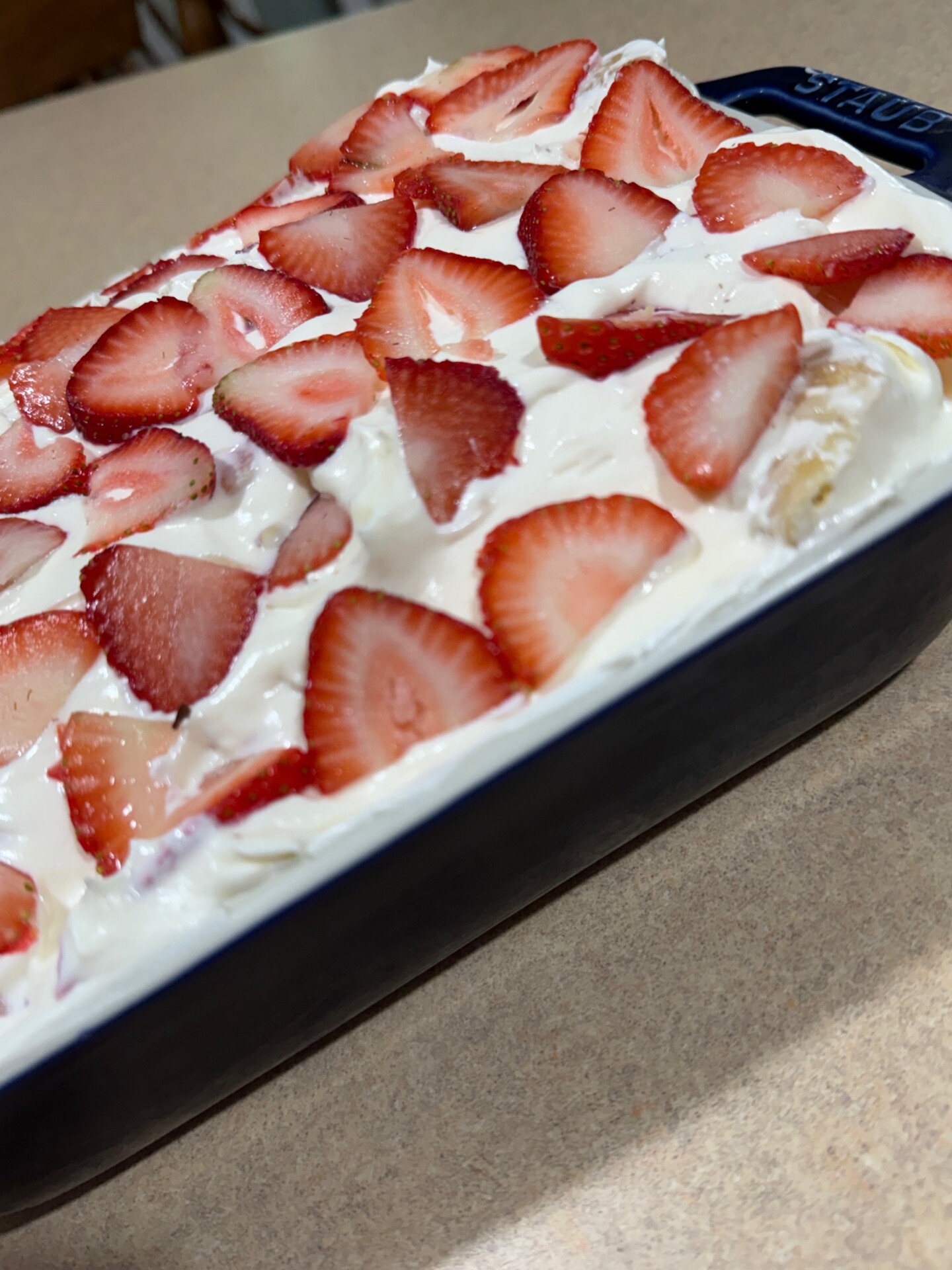 A close-up of a rectangular dish filled with a creamy dessert topped with sliced fresh strawberries, sitting on a beige countertop.