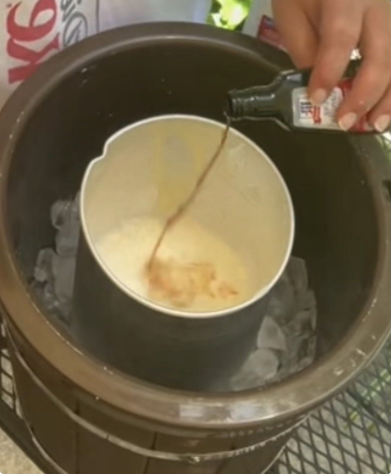 A person pours vanilla extract into an ice cream maker filled with ice and a creamy mixture, preparing homemade ice cream outdoors.