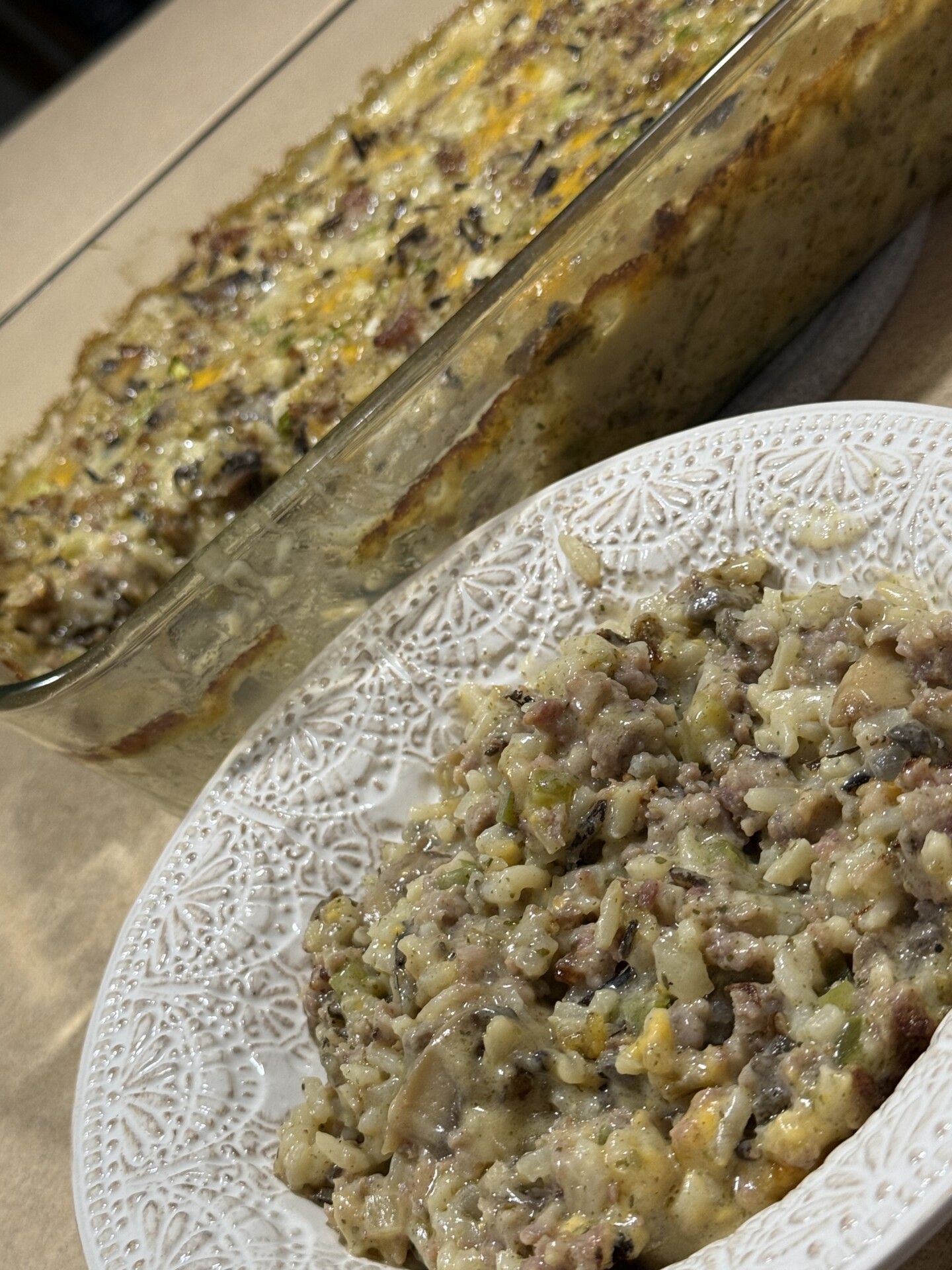 A close-up of a serving of rice and ground meat casserole with vegetables on a decorative white plate, with the casserole dish in the background.