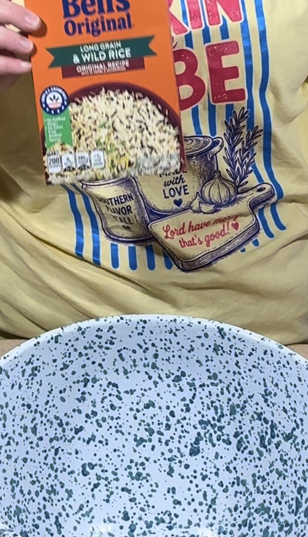 A person in a yellow shirt holds a box of Bens Original Long Grain & Wild Rice above a large white speckled mixing bowl.