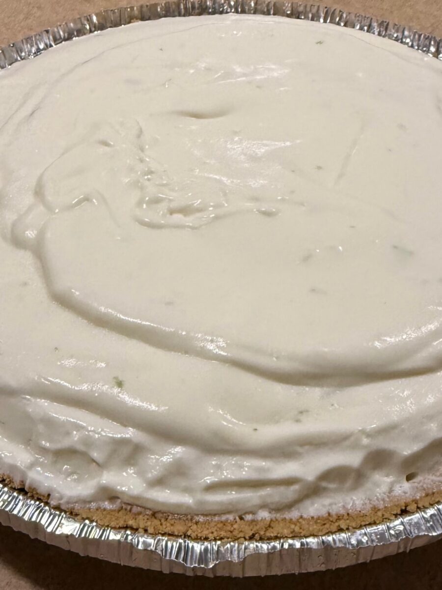 A close-up of a creamy, white pie with a graham cracker crust in an aluminum pan, sitting on a flat surface. The pie appears to be unbaked or a no-bake dessert.