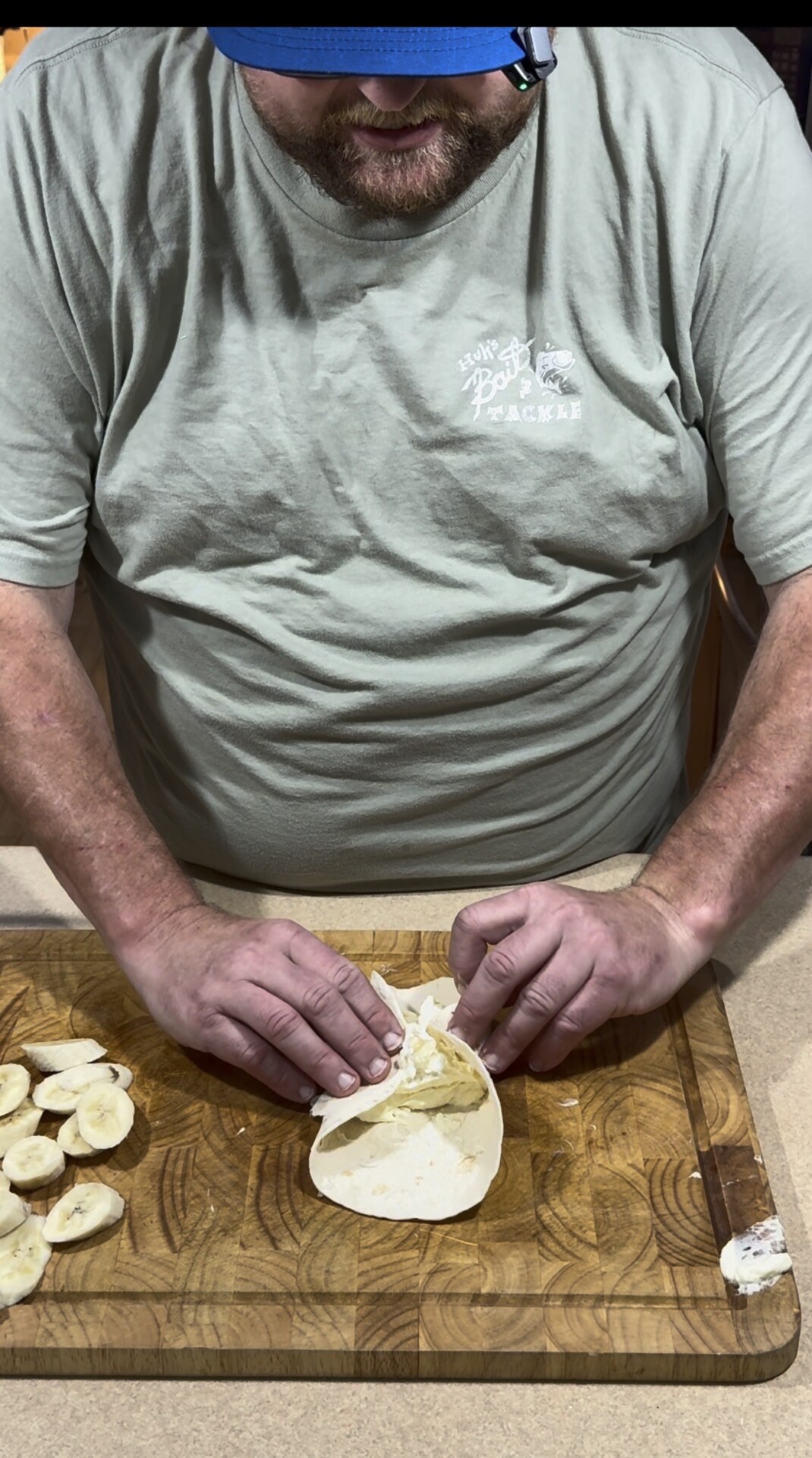A person folds a tortilla with banana slices on a wooden cutting board. More banana slices are arranged nearby.