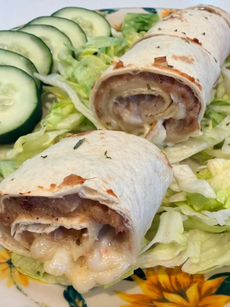 Two cheesy, baked tortillas filled with refried beans and melted cheese are served on a bed of shredded lettuce, with cucumber slices arranged on the side.