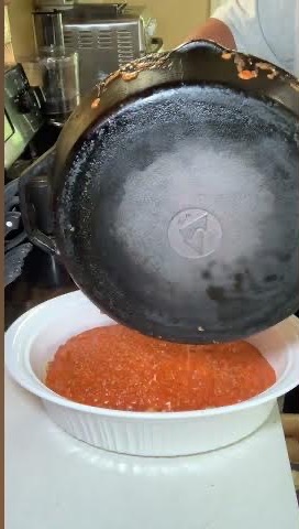 A cast iron skillet is being used to pour red sauce into a white oval dish on a kitchen counter.