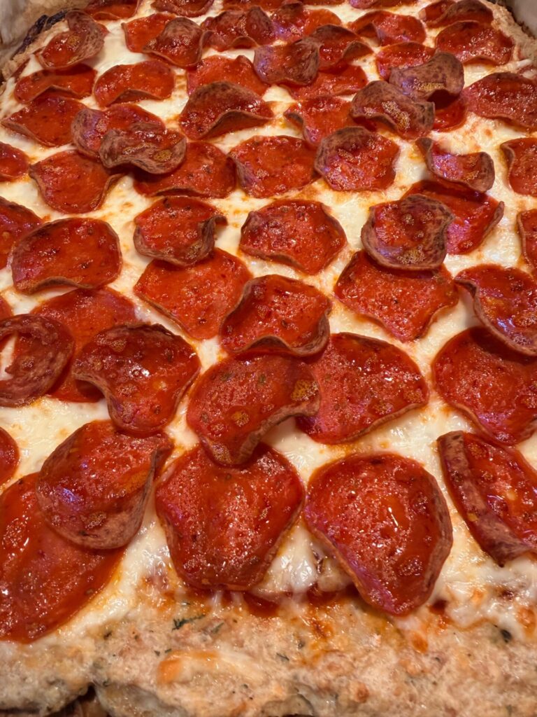 Close-up of a pizza covered with melted cheese and lots of pepperoni slices, some crisped at the edges, on a golden-brown crust.