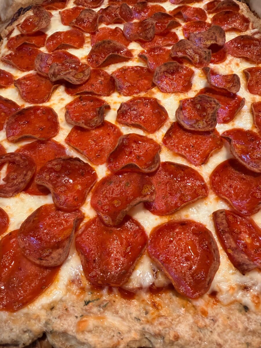 Close-up of a pizza covered with melted cheese and lots of pepperoni slices, some crisped at the edges, on a golden-brown crust.