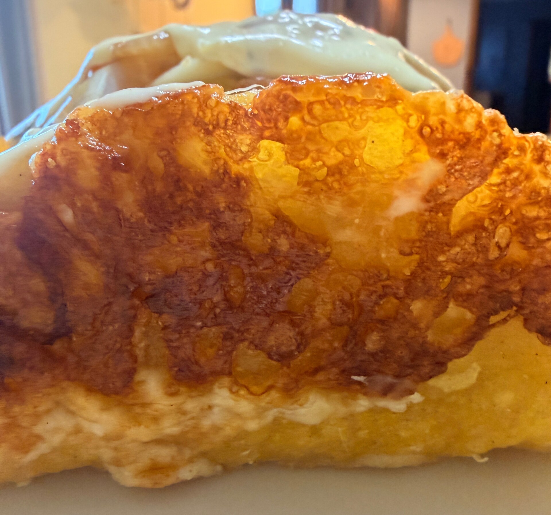 Close-up of a golden brown, crispy edge of a folded omelette, with some melted cheese visible on top, set on a plate indoors.