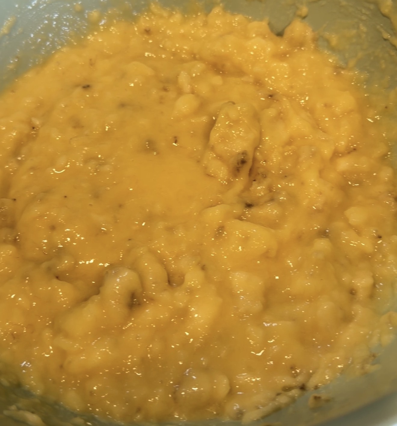 A close-up of mashed bananas in a light blue mixing bowl, showing a lumpy yellow texture.