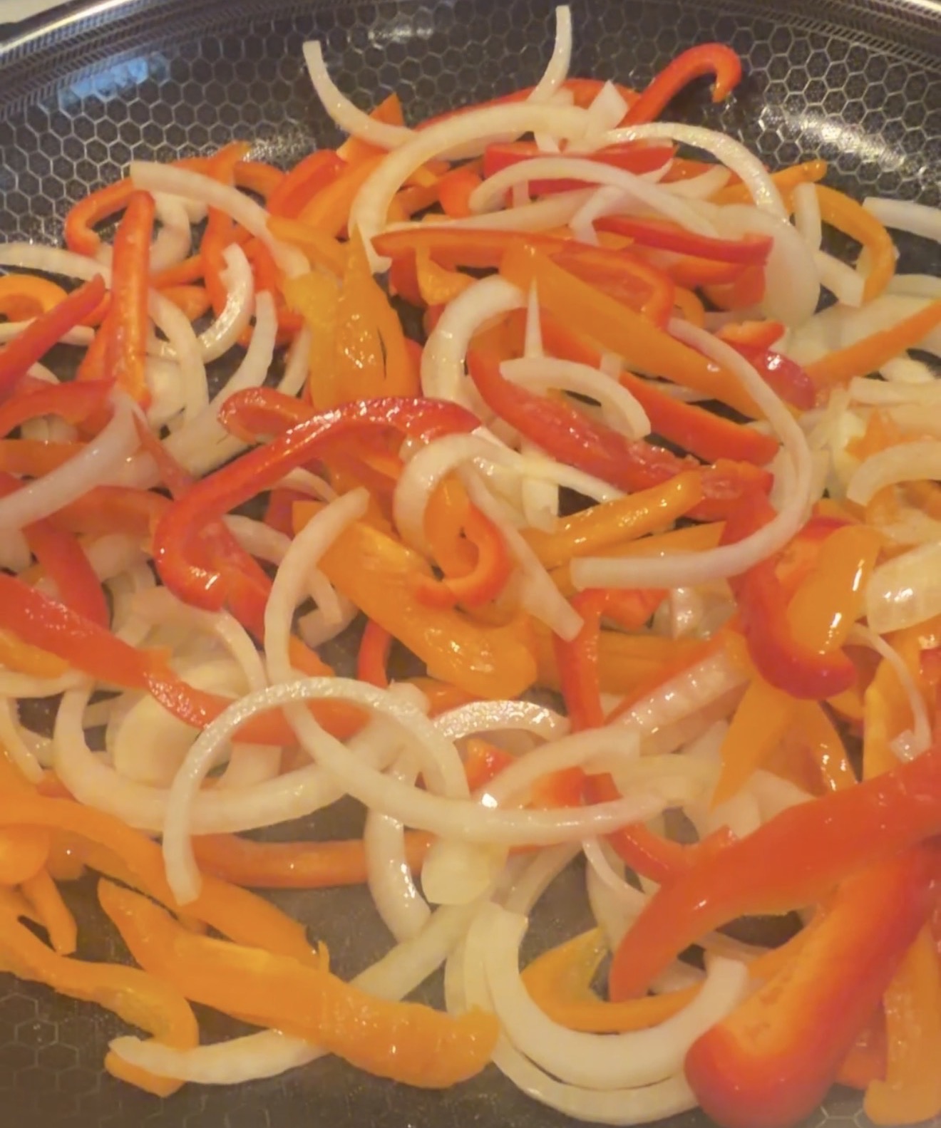 Sliced red and orange bell peppers and onions cooking in a frying pan.