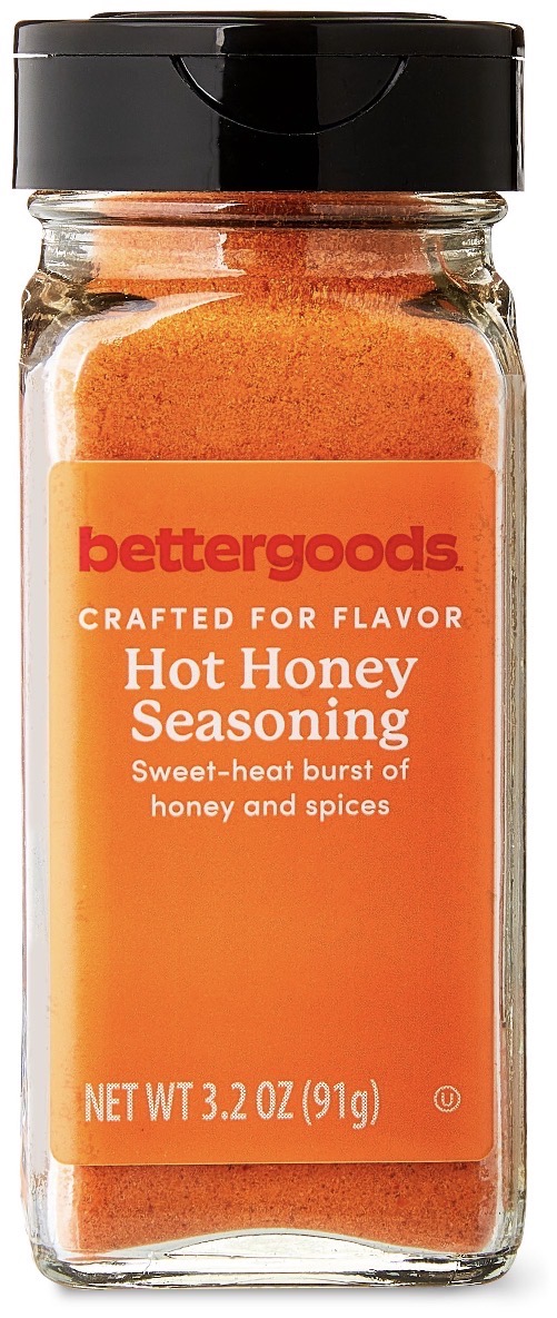 A clear bottle of bettergoods Hot Honey Seasoning, showing bright orange powder inside. The label reads “Sweet-heat burst of honey and spices” and indicates a net weight of 3.2 oz (91g).