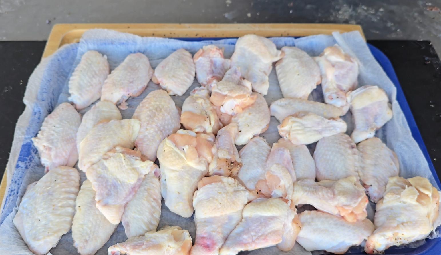 Raw chicken wings arranged on a blue tray lined with paper towels, ready for preparation or cooking.