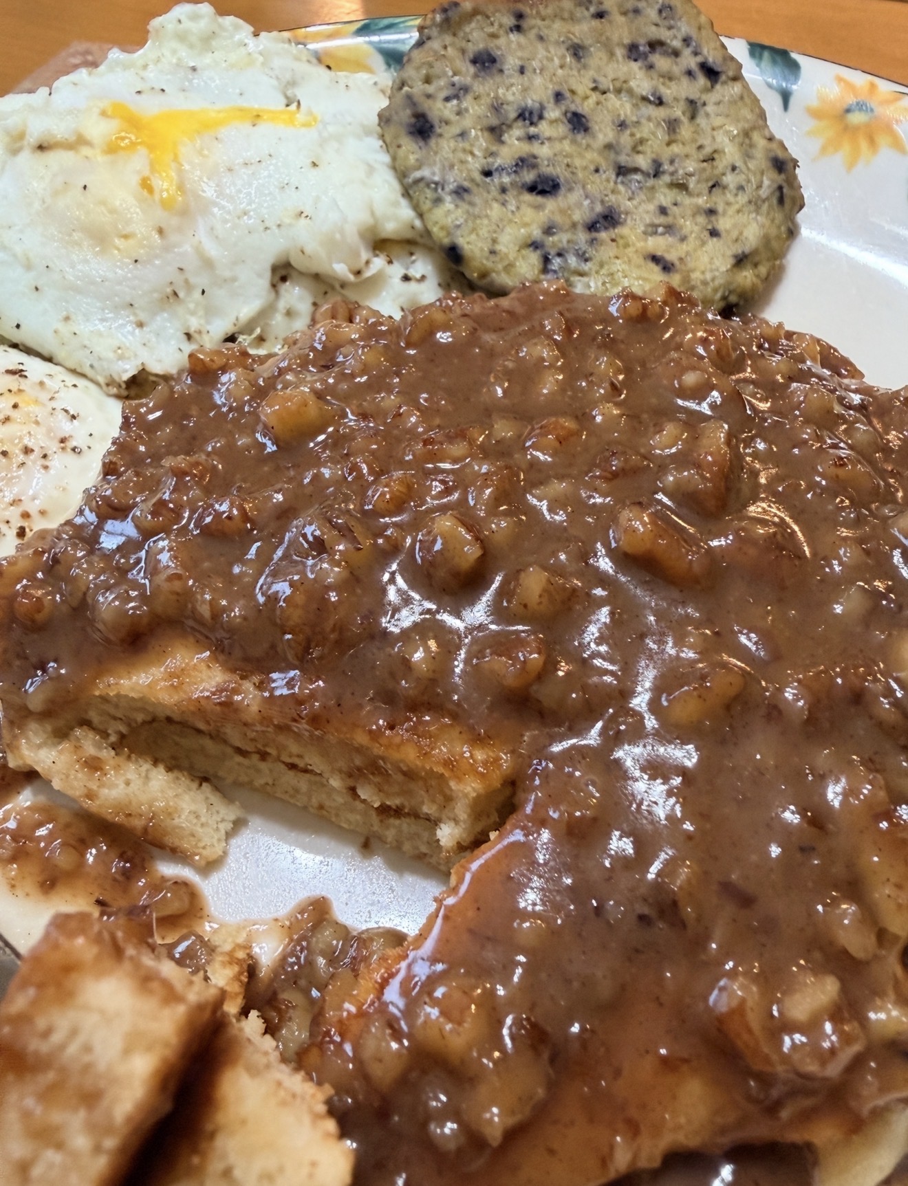 A plate with eggs, a biscuit topped with brown sausage gravy, a biscuit with slices removed, and a round piece of sausage.