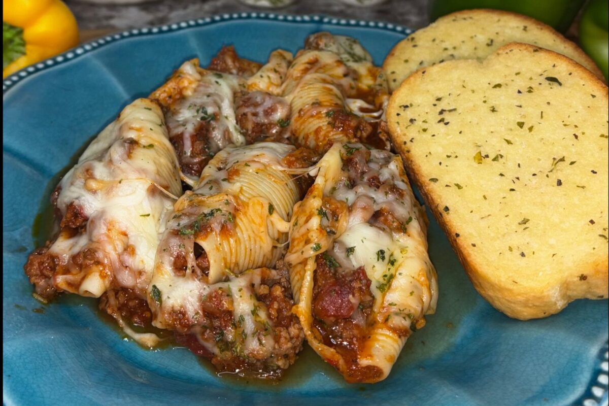 Stuffed pasta shells filled with ground meat and topped with melted cheese are served with two slices of garlic bread on a blue plate.
