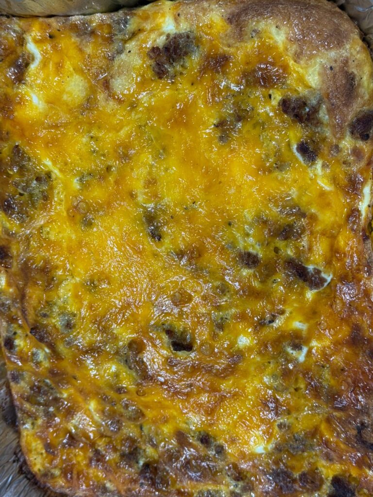 A close-up of a baked casserole with a golden, bubbly cheese layer on top, featuring browned spots and a slightly crispy edge.