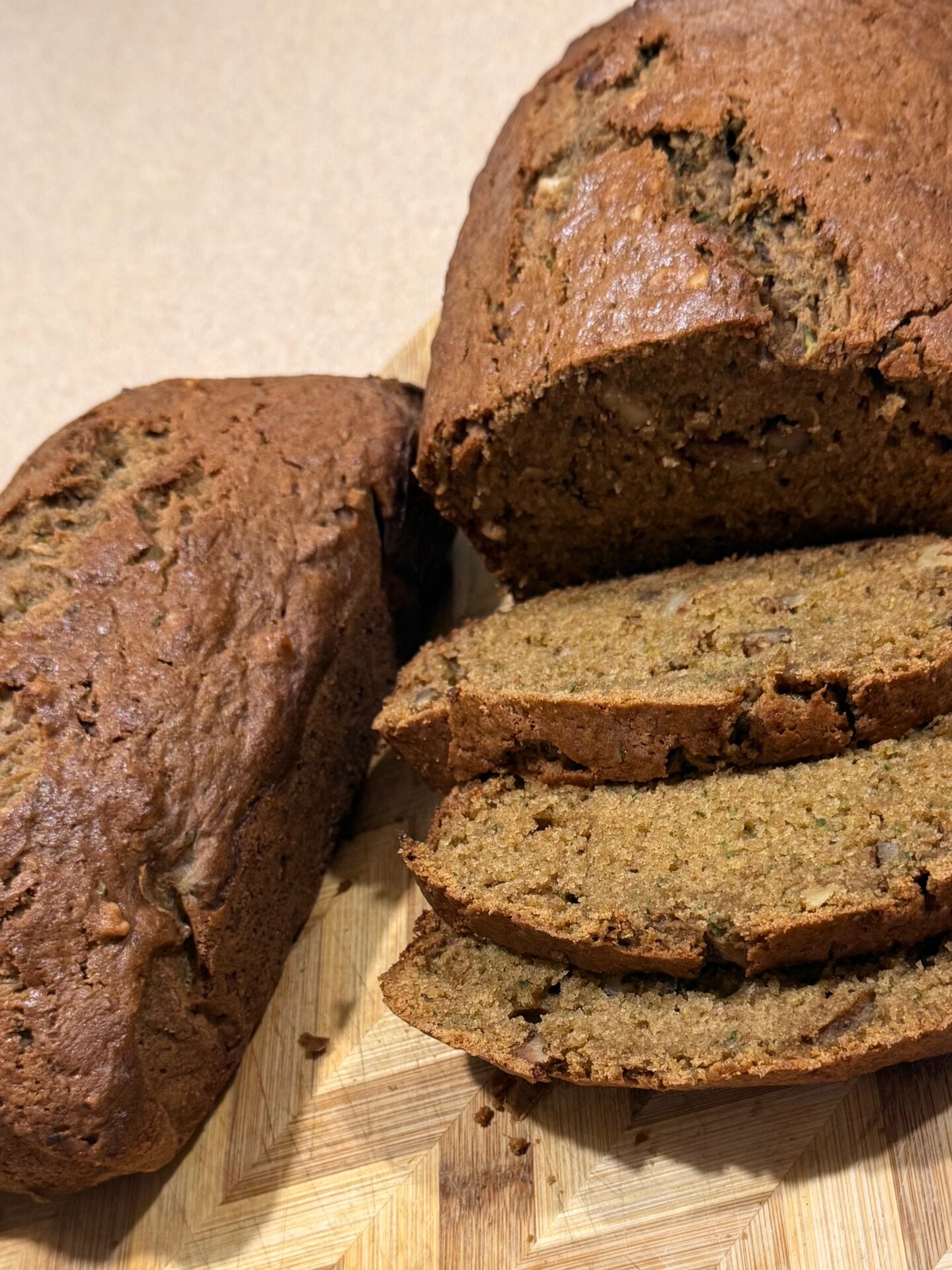 Sliced homemade banana bread sits on a wooden cutting board. The loaf is moist with a golden-brown crust, and three slices are cut and fanned out beside the remaining bread.