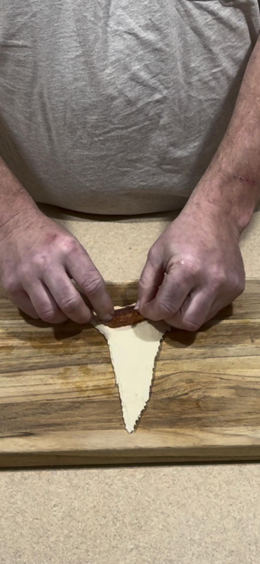 A person rolls up a piece of dough with a filling on a wooden board, with only their hands and torso visible.