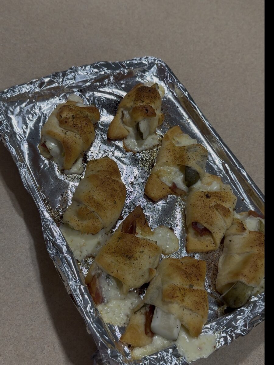 Baked crescent rolls filled with melted cheese and other ingredients, arranged on a foil-lined baking sheet placed on a beige countertop.