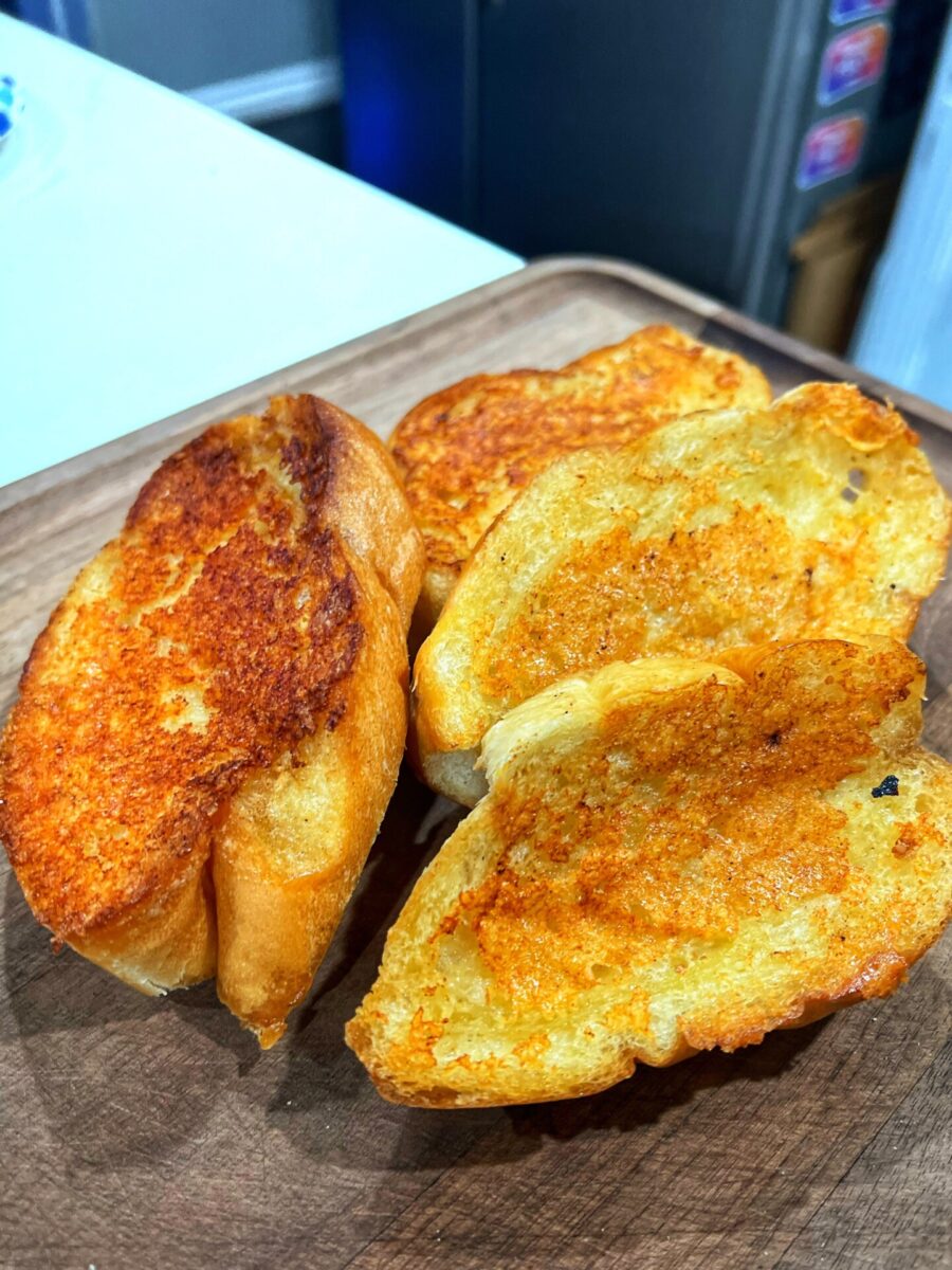 Four slices of golden-brown toasted bread with crispy edges are placed on a wooden board, ready to serve.